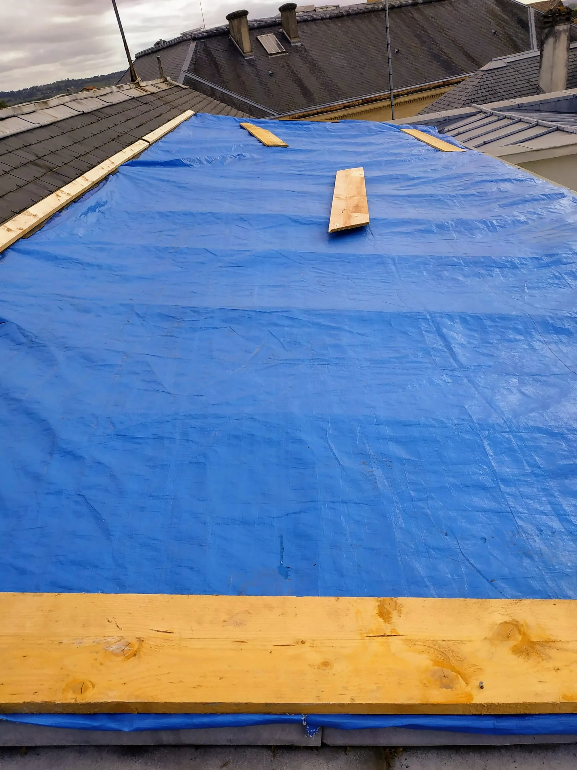 Toiture en rénovation protégée par une bâche bleue lors de travaux de couverture