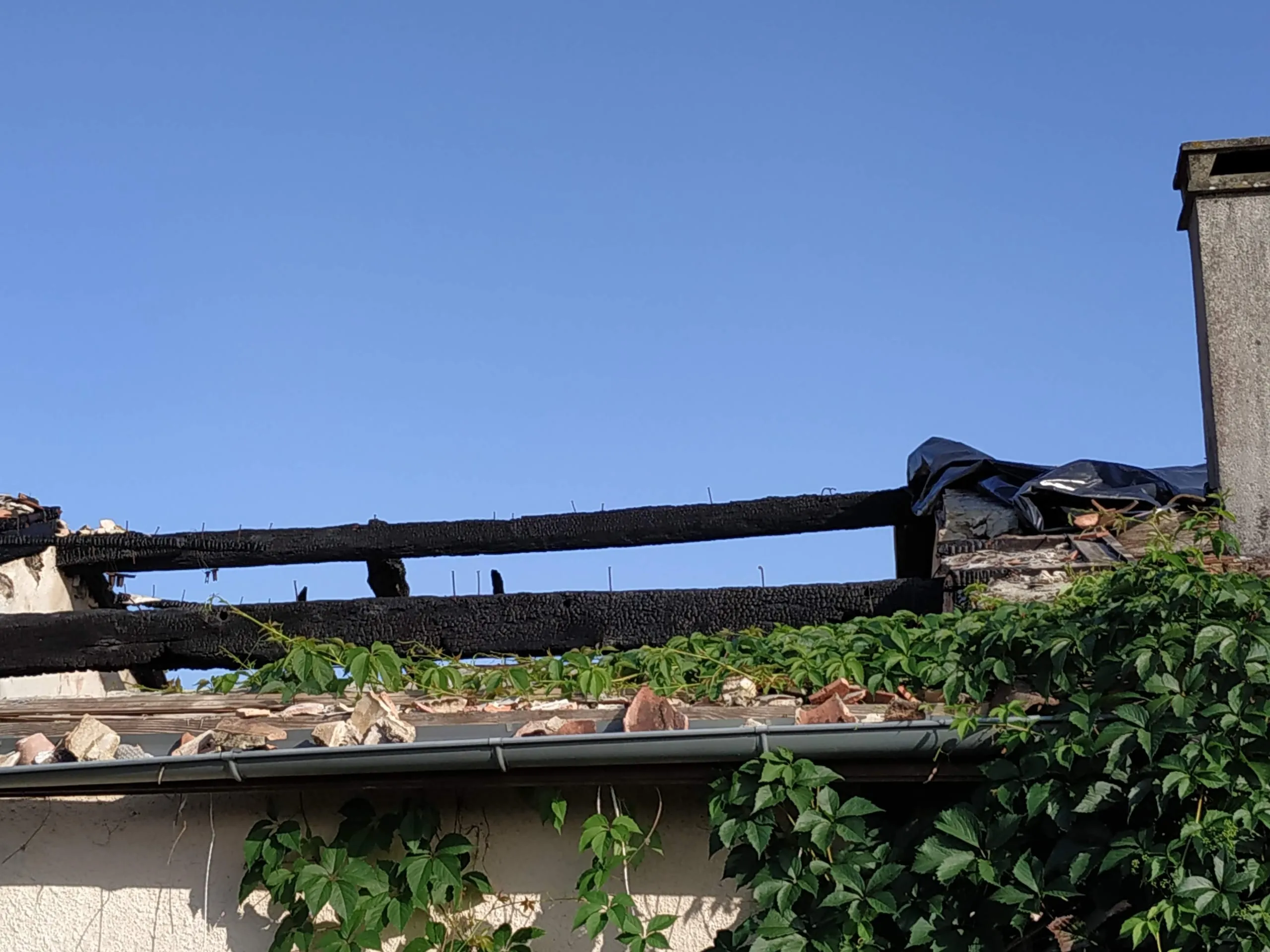 Toiture fortement endommagée avec tuiles cassées, éléments noircis et bâche provisoire