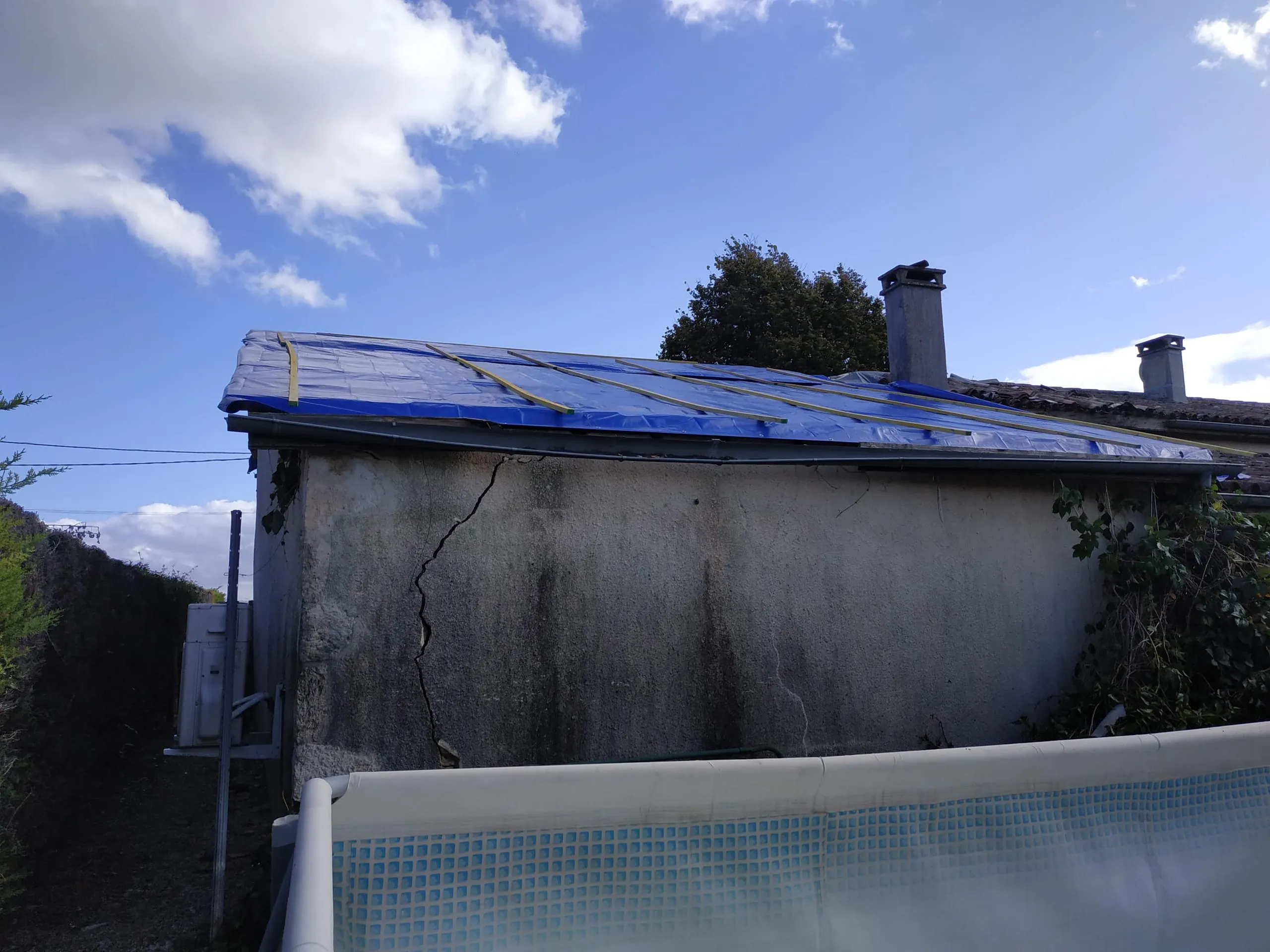 Bâche de protection fixée sur une toiture avec deux cheminées
