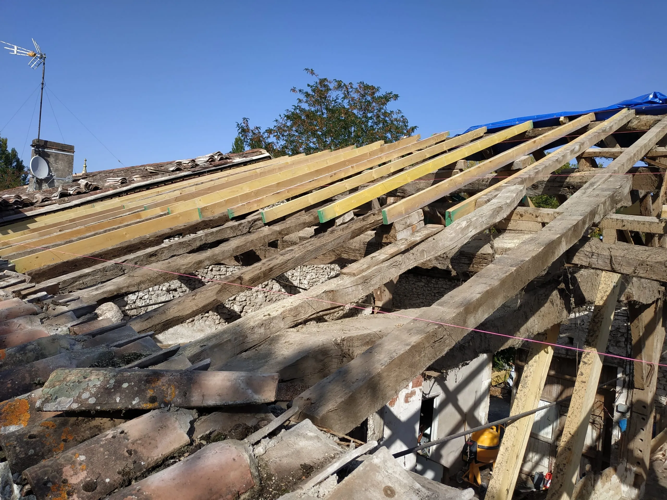 Charpente ancienne apparente avec pièces de bois neuves et tuiles déposées