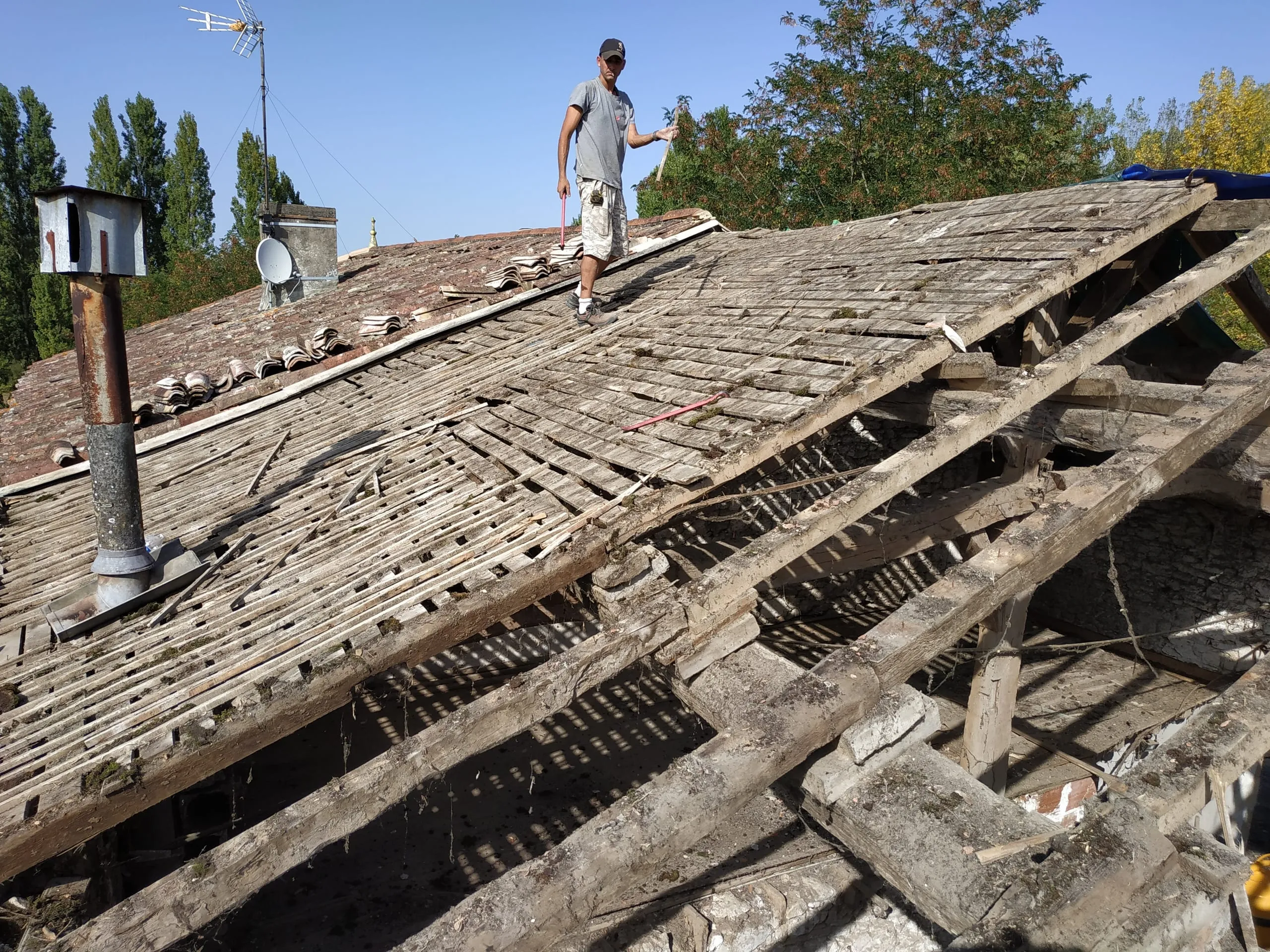 Couvreur sur une toiture ancienne partiellement déposée avec charpente et liteaux apparents