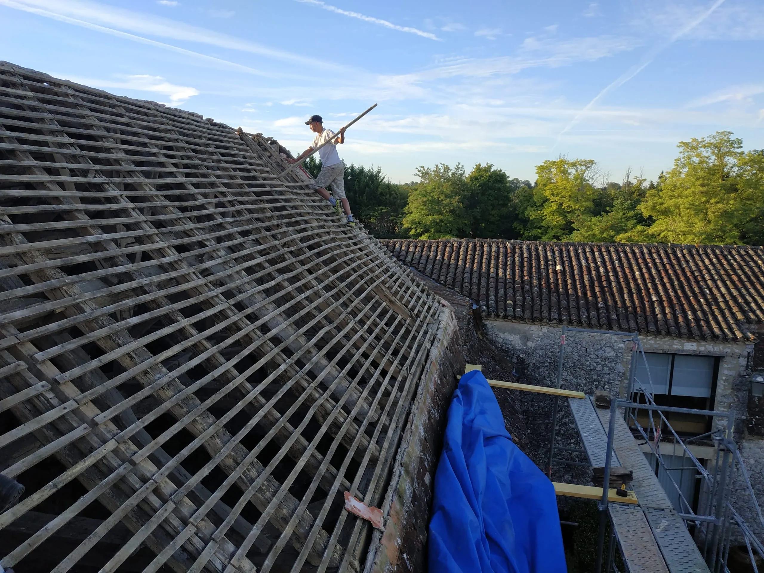 Couvreur travaillant sur une toiture ancienne avec liteaux apparents et échafaudage