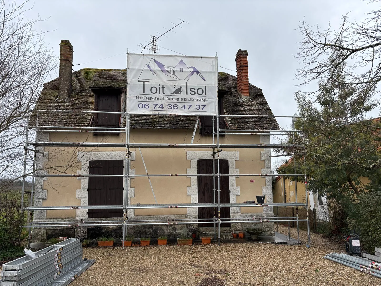 Échafaudage avec garde-corps installé devant une maison ancienne à toiture en petites tuiles