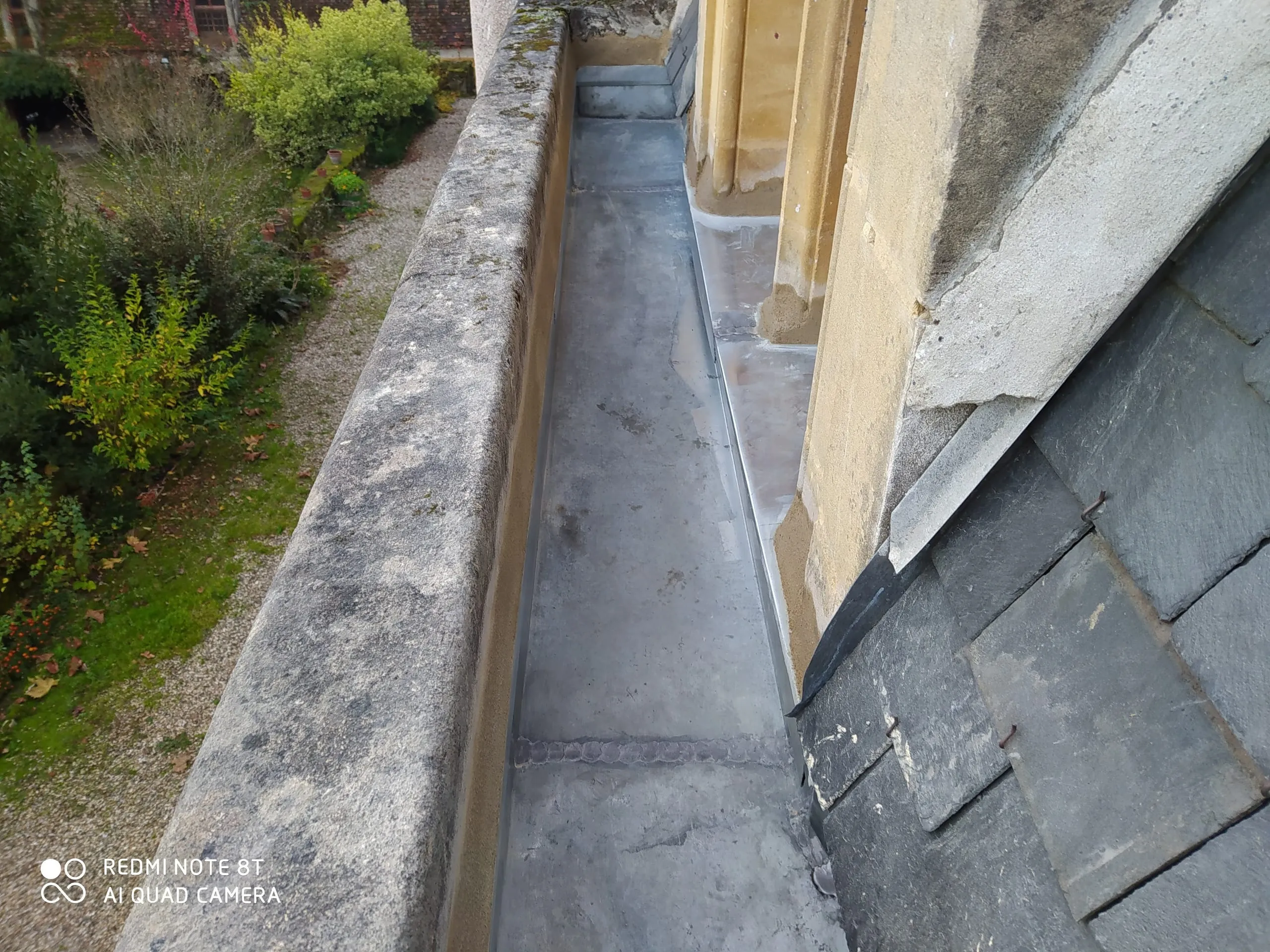 Gouttière en zinc et raccord le long d’une toiture en ardoise au-dessus d’un jardin
