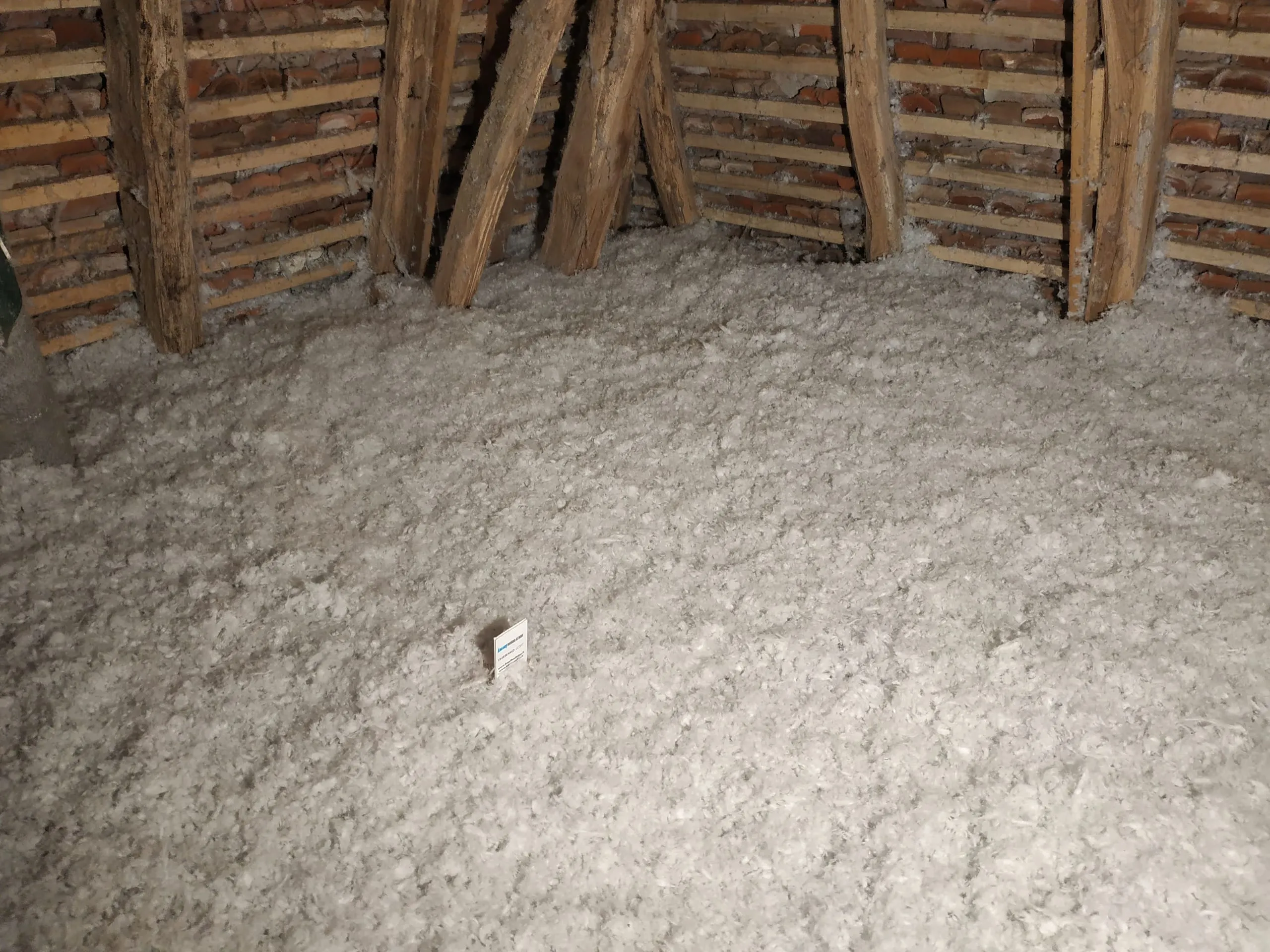 Isolant soufflé au sol de combles sous une charpente ancienne et des murs en briques