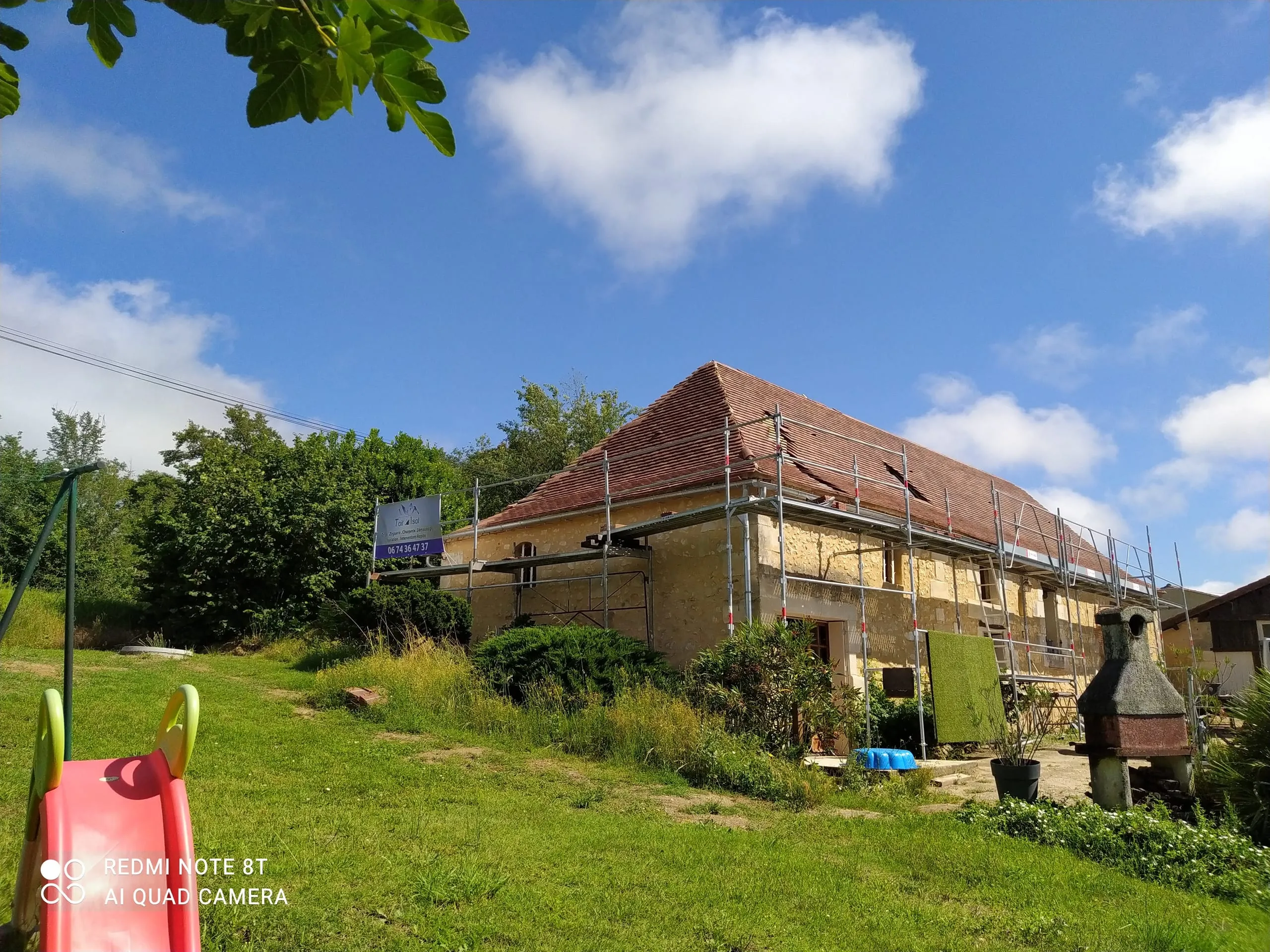 Maison ancienne en pierre avec toiture en tuiles en rénovation et échafaudage dans le jardin