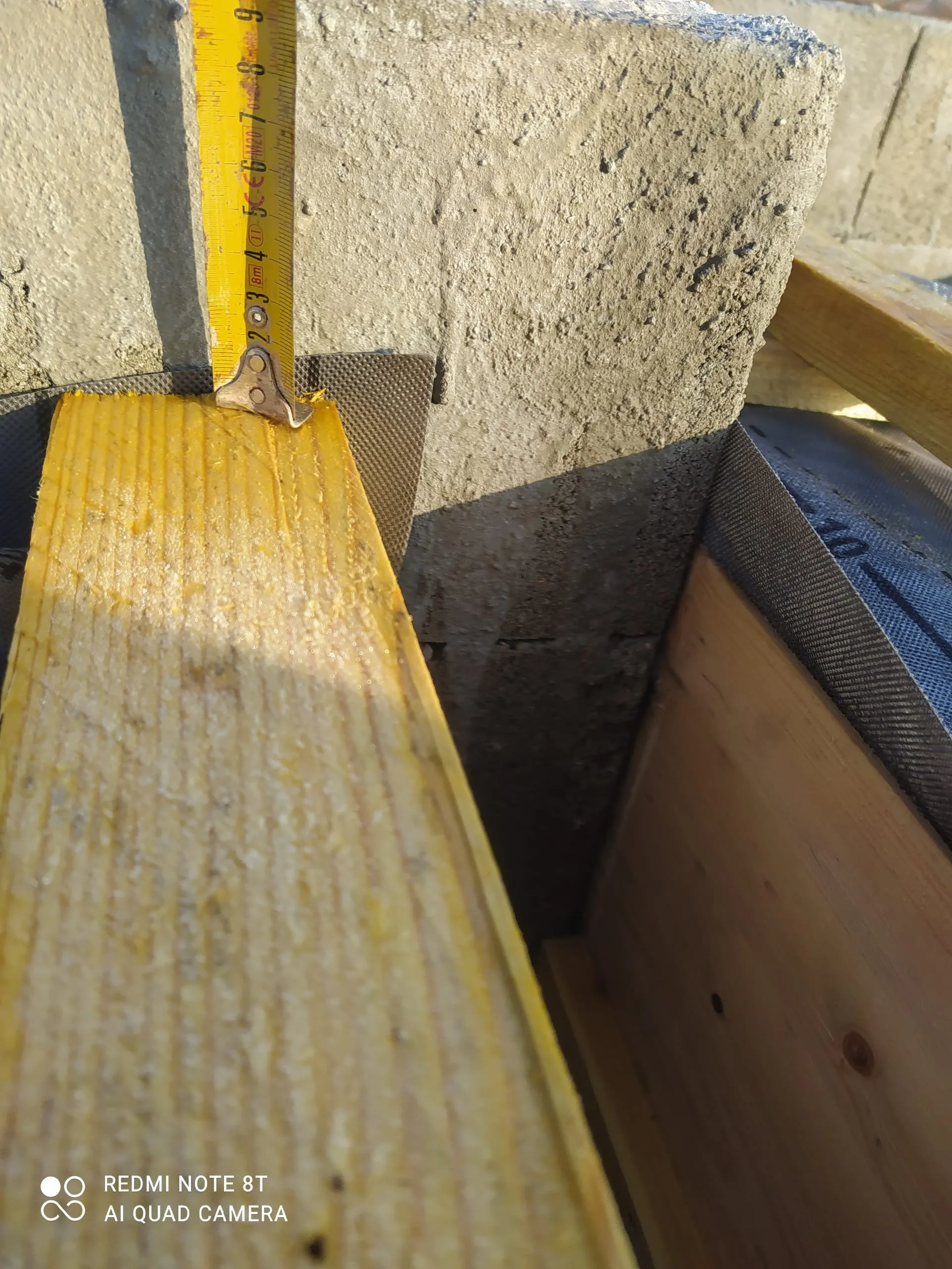 Mètre ruban posé contre un isolant jaune dans une structure de toiture en bois