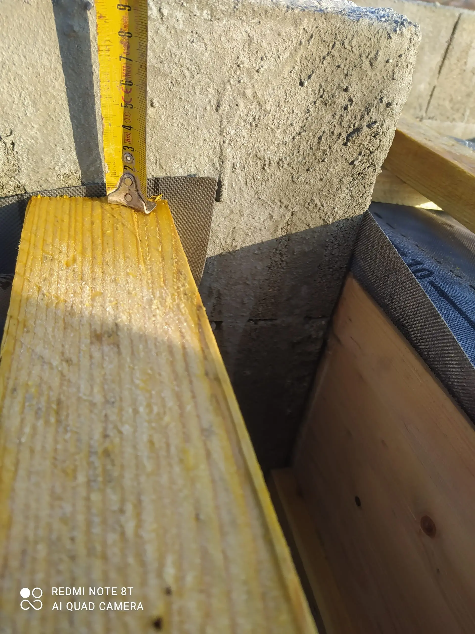 Mètre ruban posé contre un isolant jaune dans une structure de toiture en bois