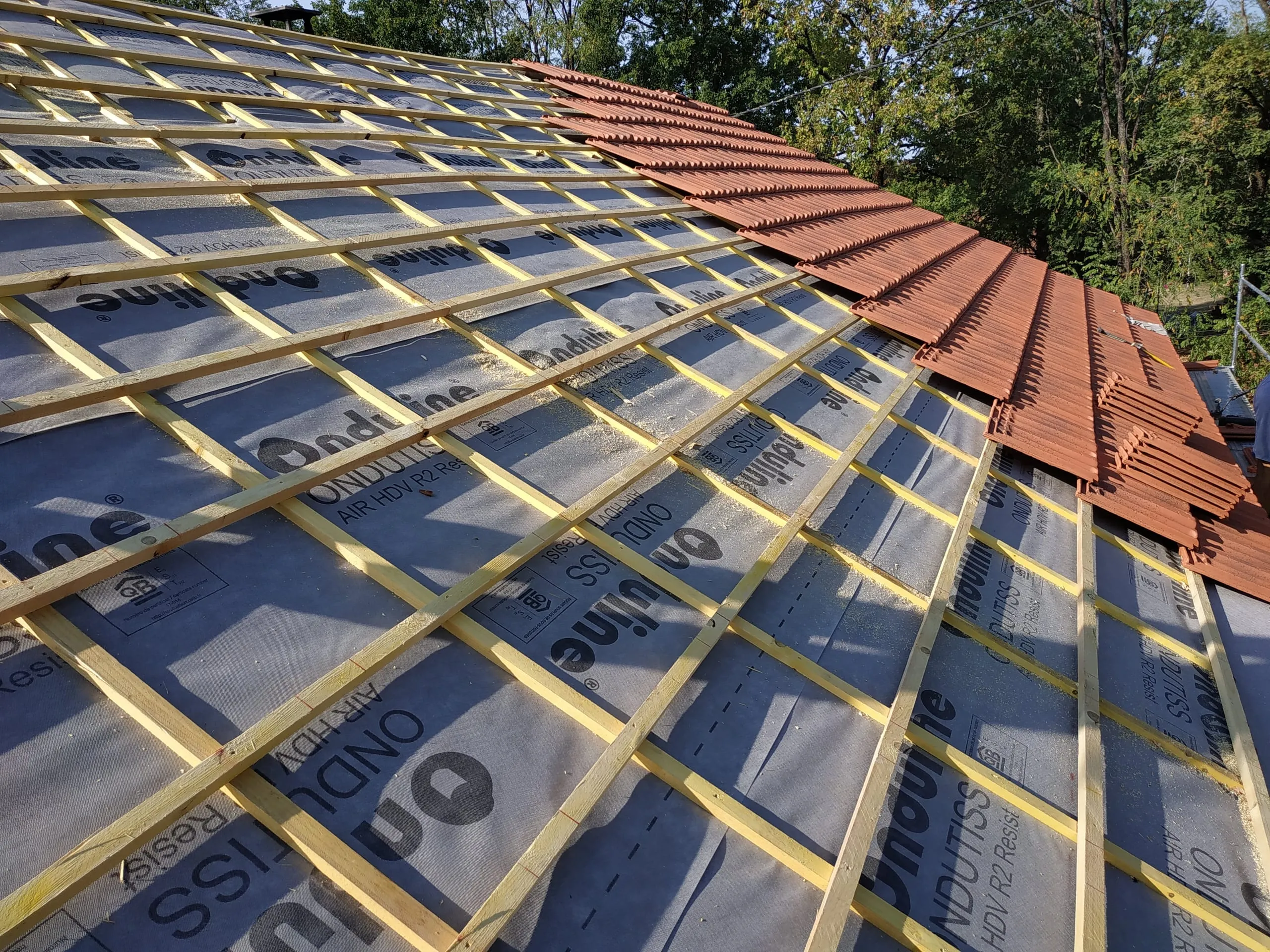 Écran sous-toiture et liteaux en bois avec pose progressive de tuiles rouges
