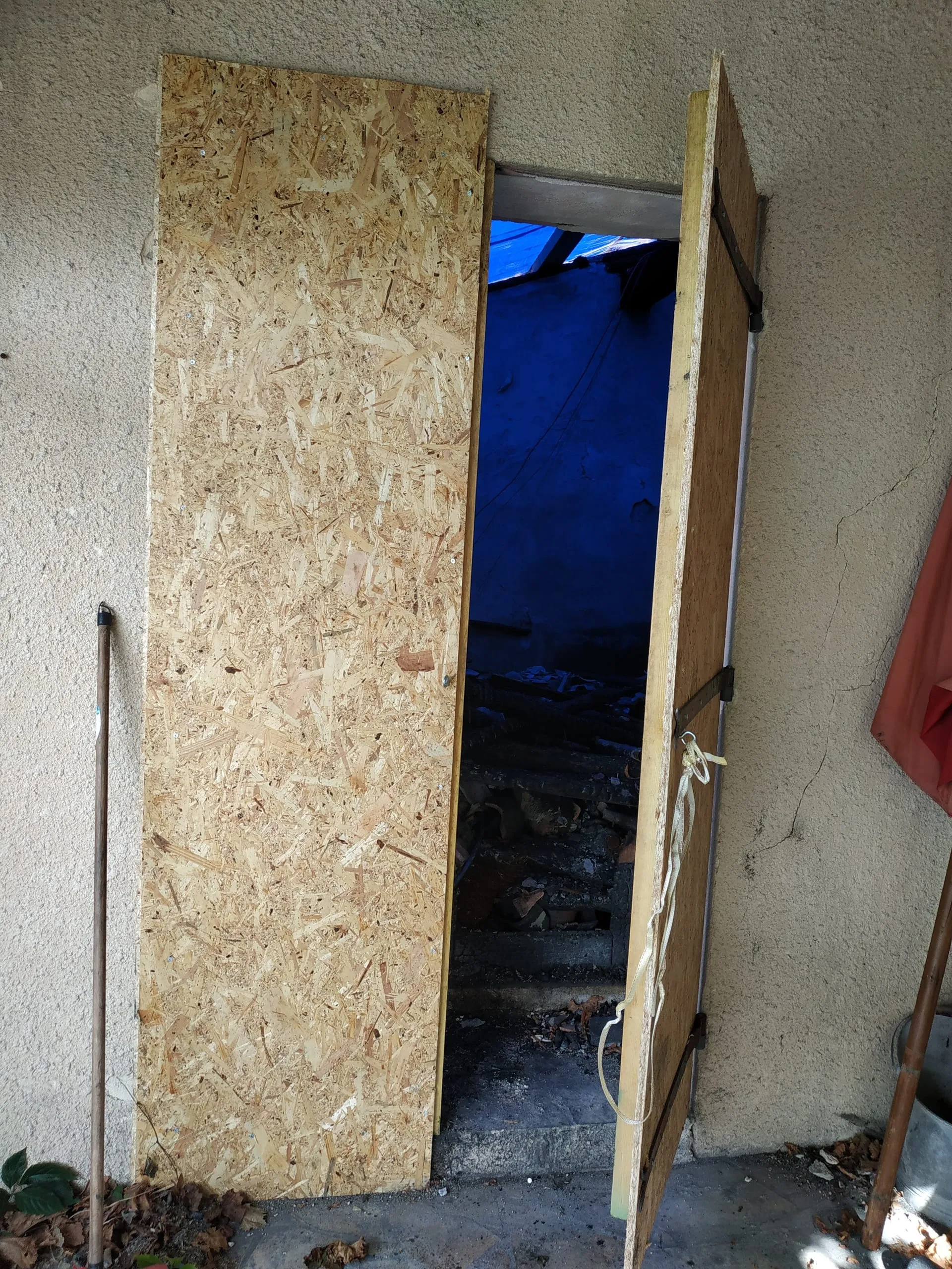 Ouverture de toiture protégée provisoirement par des panneaux en bois et une bâche bleue