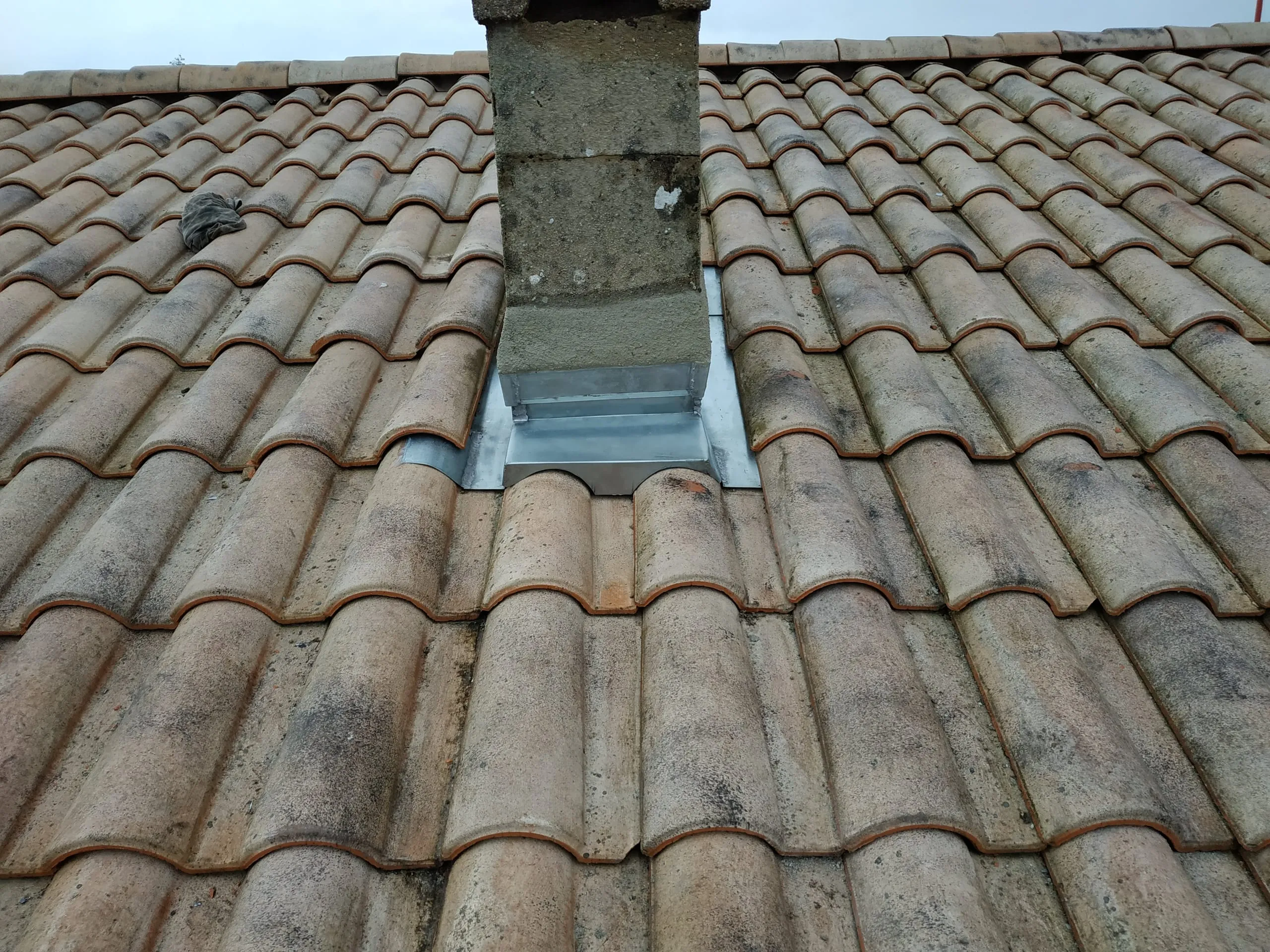 Raccord en zinc autour d’une cheminée sur une toiture en tuiles anciennes