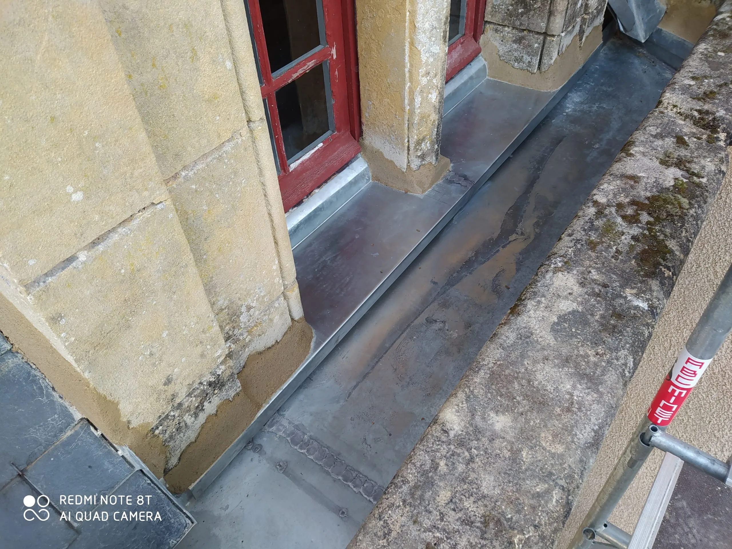Raccords en zinc autour d’une fenêtre de toiture sur une façade en pierre avec échafaudage