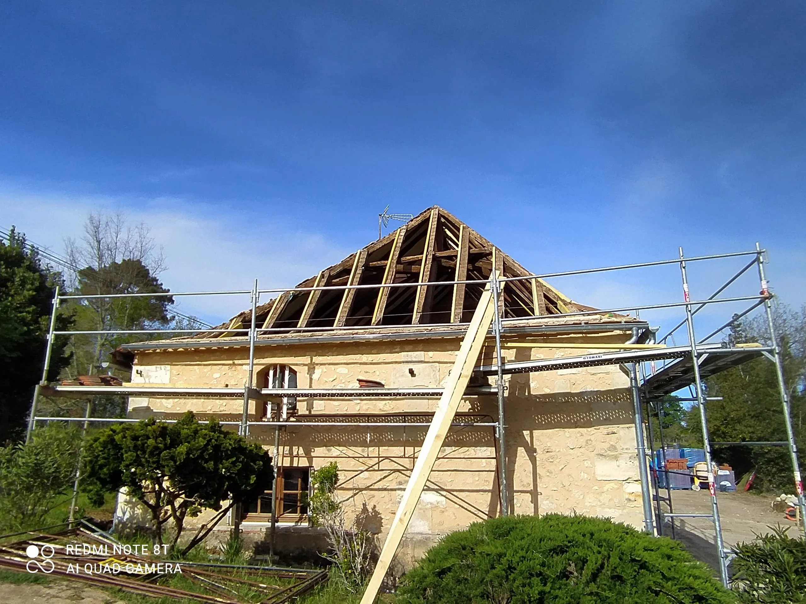 Maison en pierre avec toiture déposée, charpente apparente et échafaudage