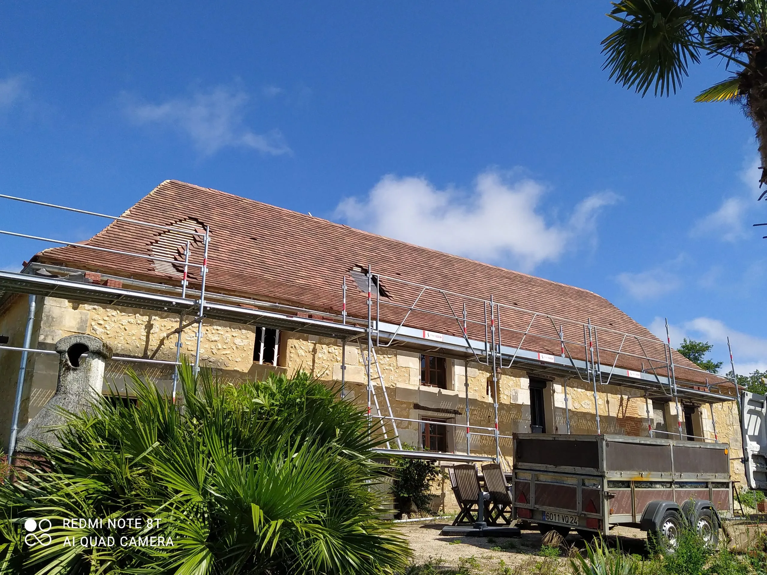 Longue toiture en tuiles en cours de rénovation sur une maison en pierre entourée d’un échafaudage