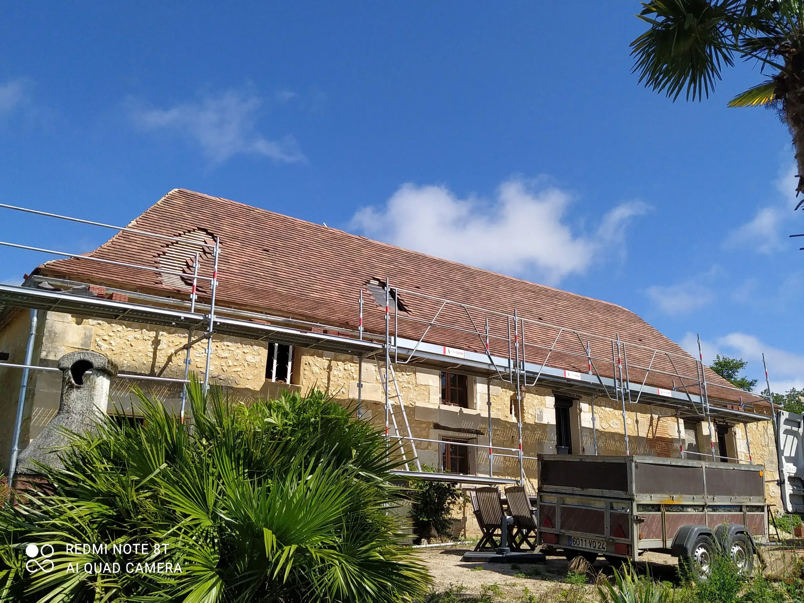 Longue toiture en tuiles en cours de rénovation sur une maison en pierre entourée d’un échafaudage