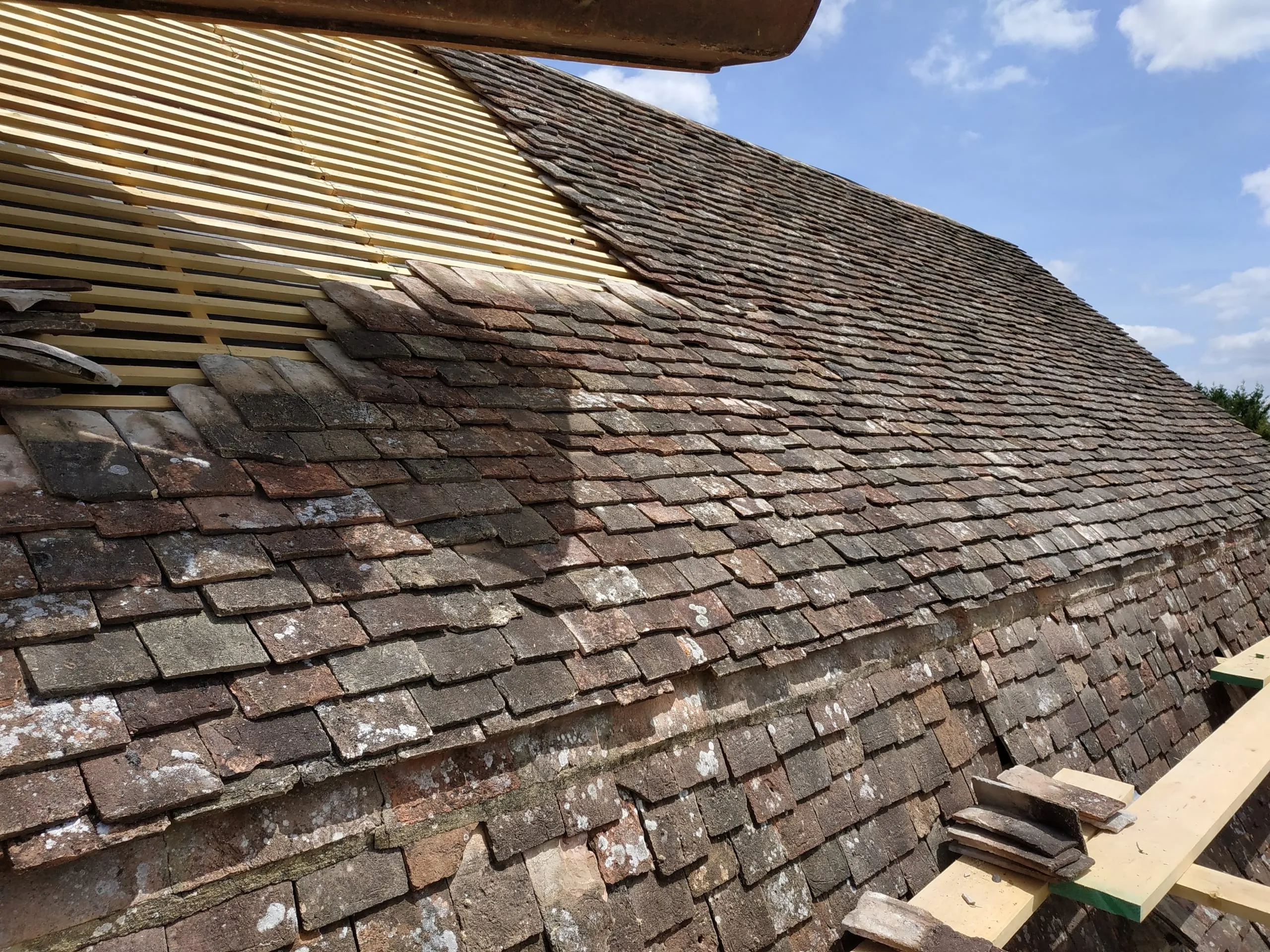 Toiture ancienne en tuiles plates partiellement découverte, avec liteaux en bois apparents