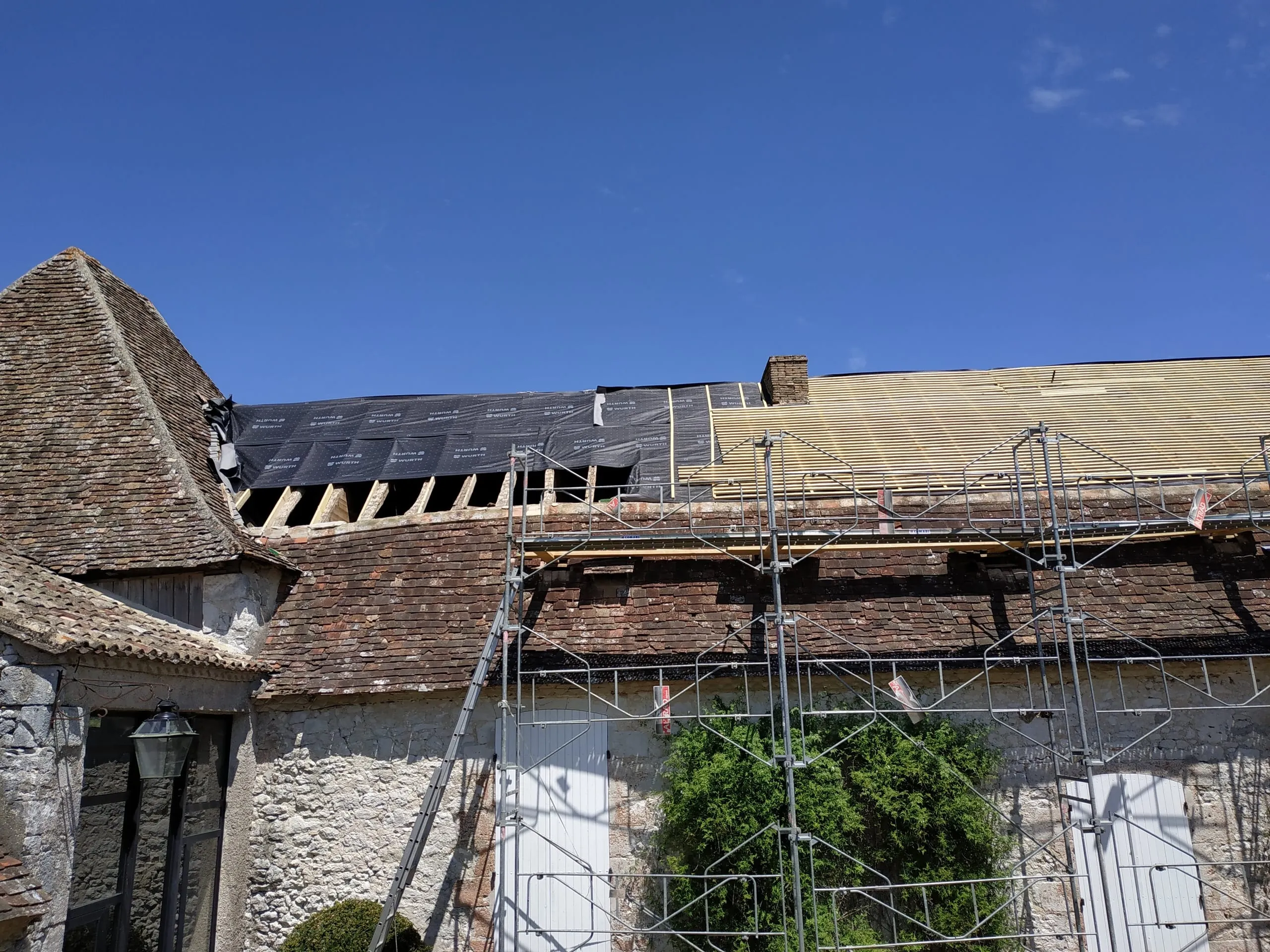 Bâtiment ancien en pierre avec échafaudage, écran sous-toiture et liteaux visibles pendant la rénovation