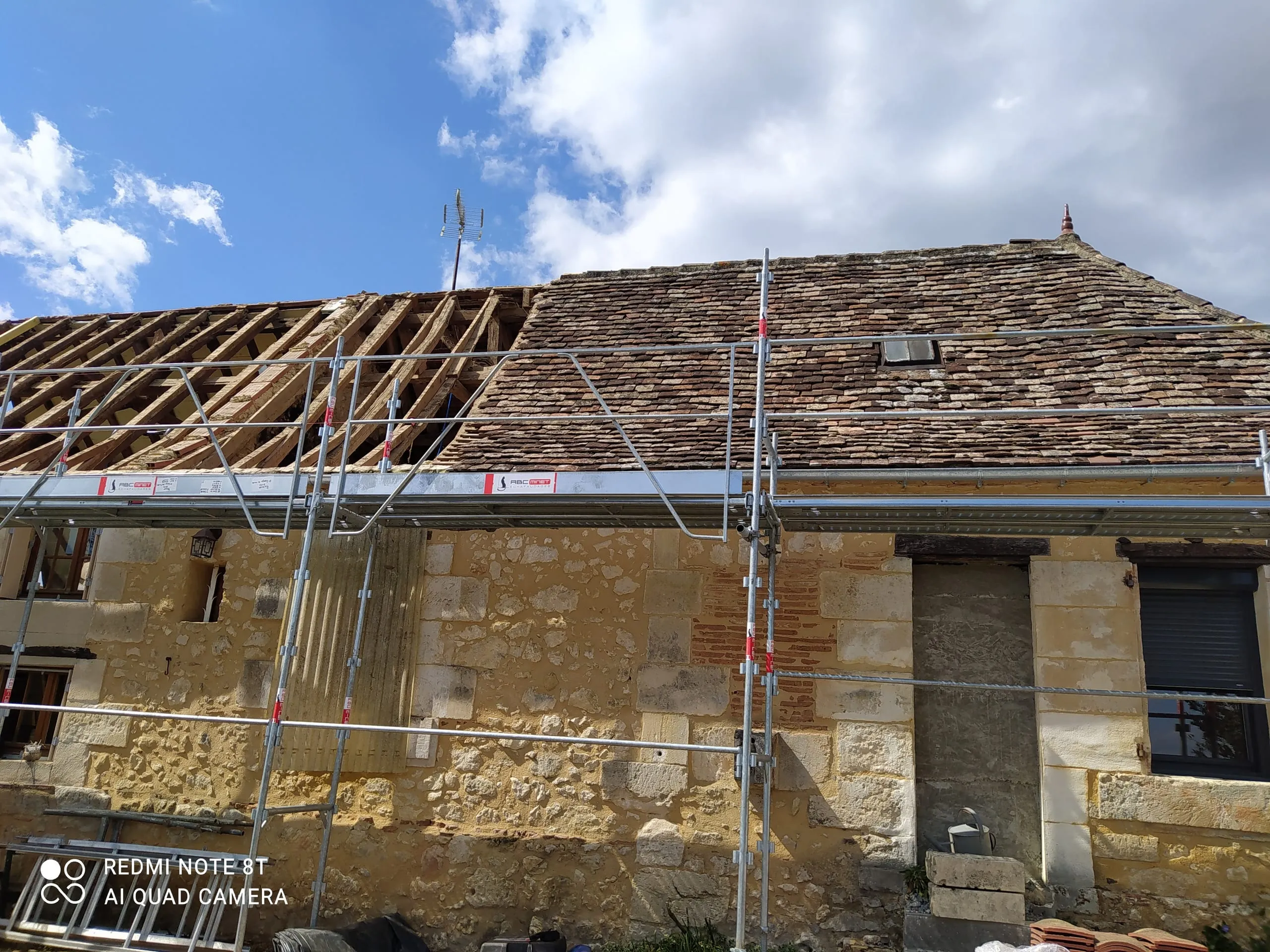 Rénovation d'une toiture sur une maison ancienne en pierre avec charpente apparente et échafaudage