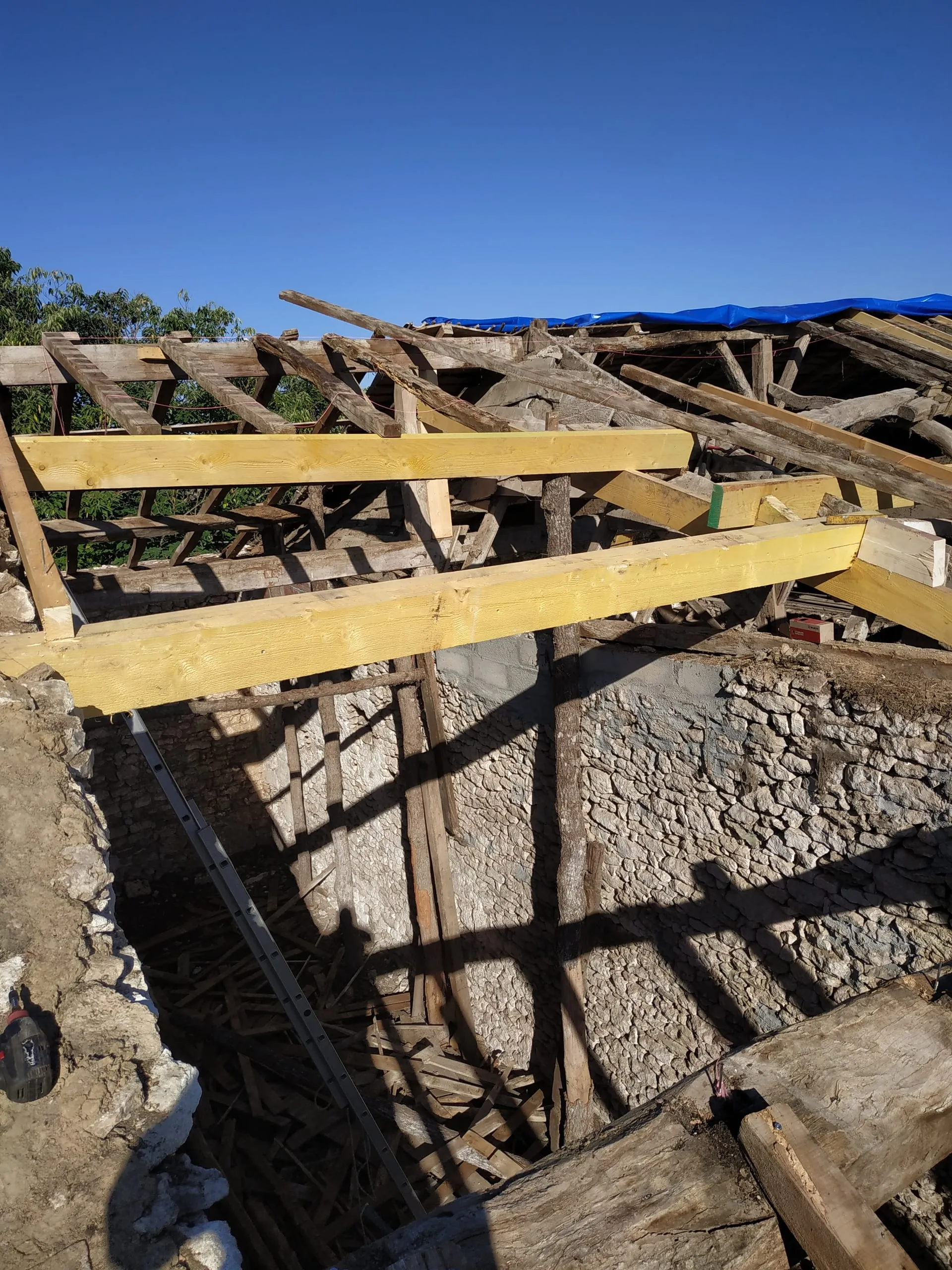 Poutres neuves posées parmi les bois anciens au-dessus de murs en pierre