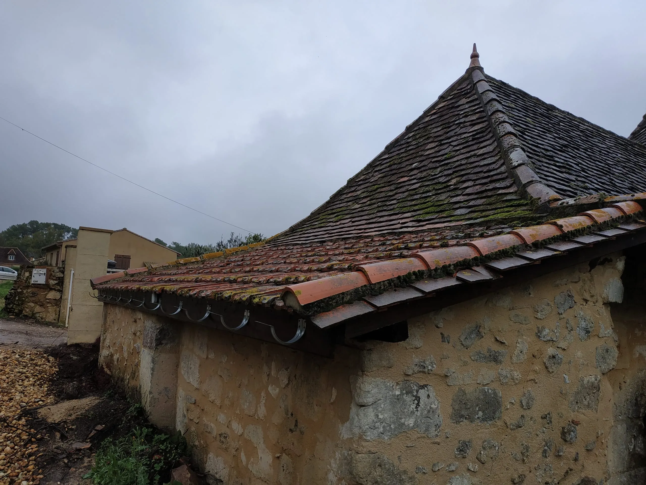 Toiture ancienne en tuiles plates et tuiles canal couverte de mousse avec gouttière métallique