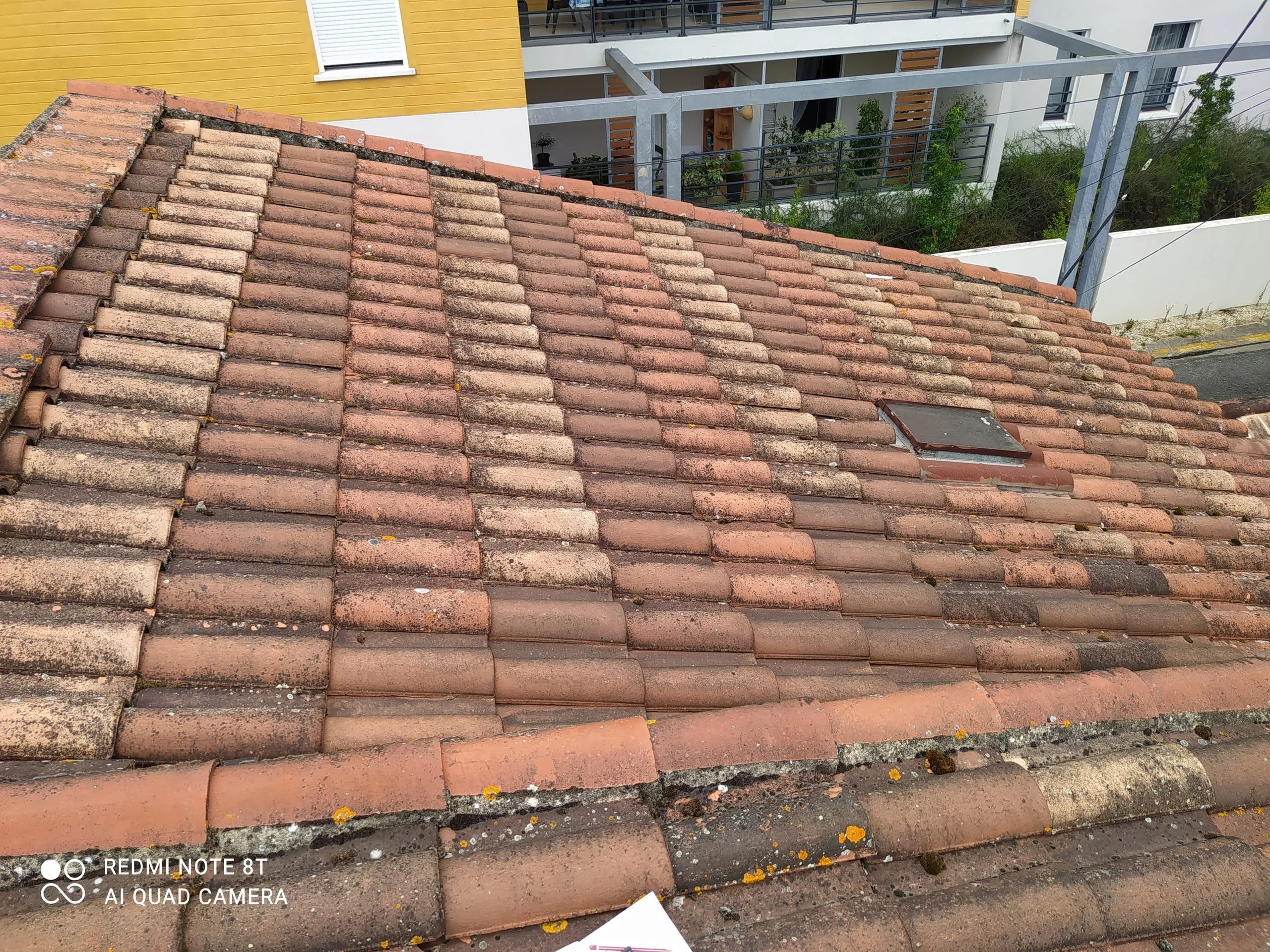 Toiture en tuiles anciennes avec fenêtre de toit et traces de mousse