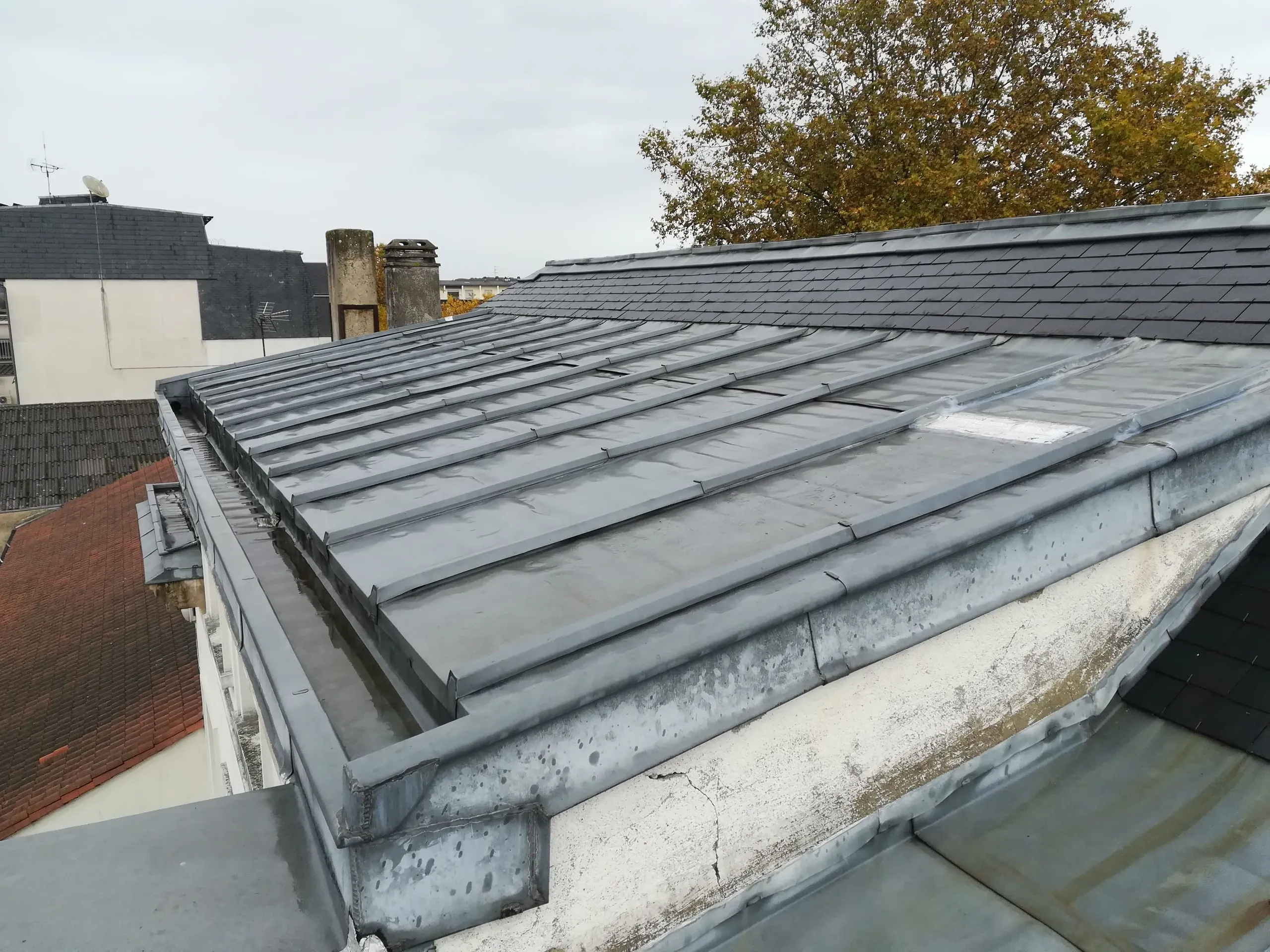Toiture en zinc et ardoise avec gouttières et cheminées, vue depuis un toit