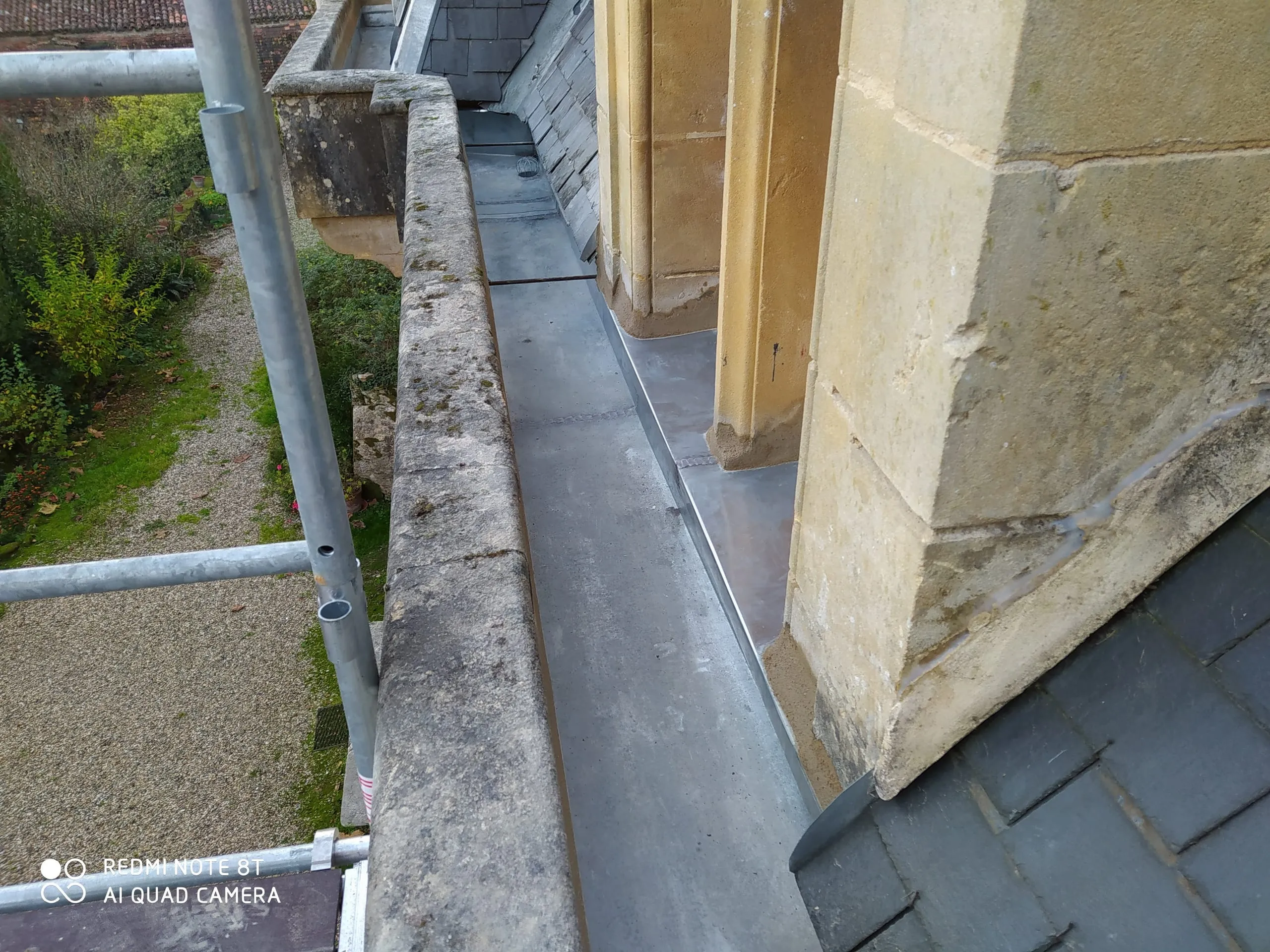 Gouttière et raccords en zinc le long d’une toiture en ardoise et d’un mur en pierre