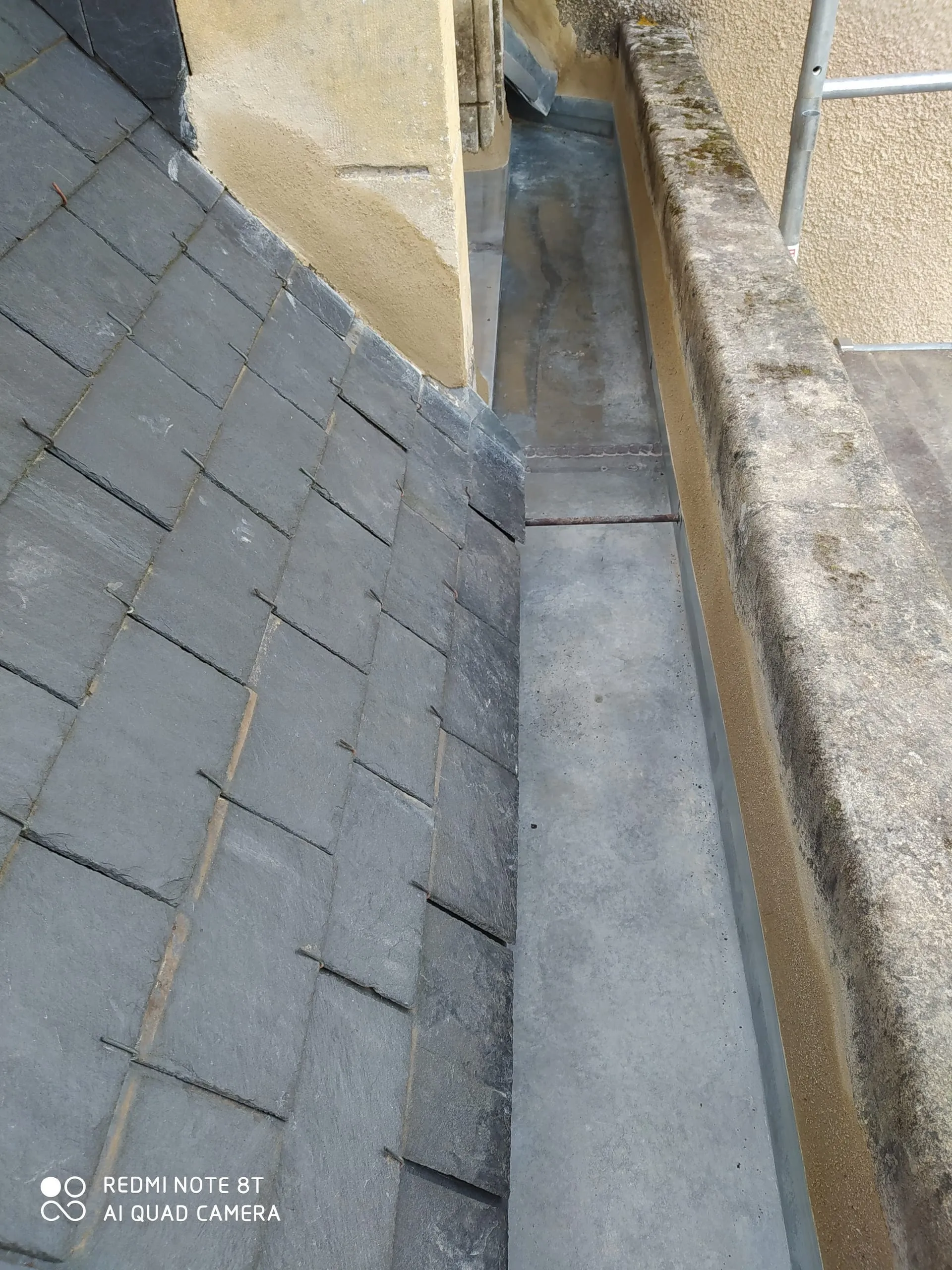 Noue en zinc entre une toiture en ardoise et un mur avec des outils posés sur un échafaudage