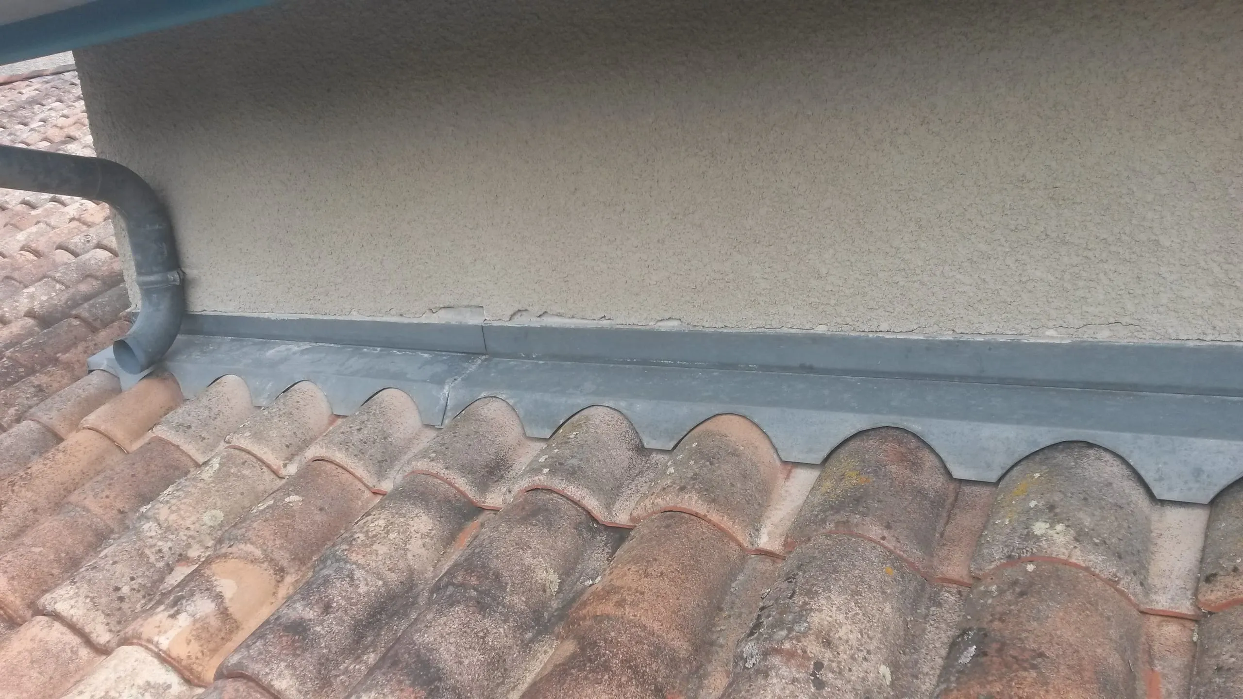 Raccord en zinc entre un mur enduit, une descente d’eau et des tuiles anciennes